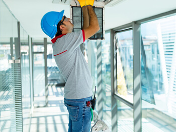 Fluidics handyman technician servicing equipment above a ceiling vent