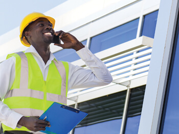 Man wearing a construction vest and hat talking on a phone